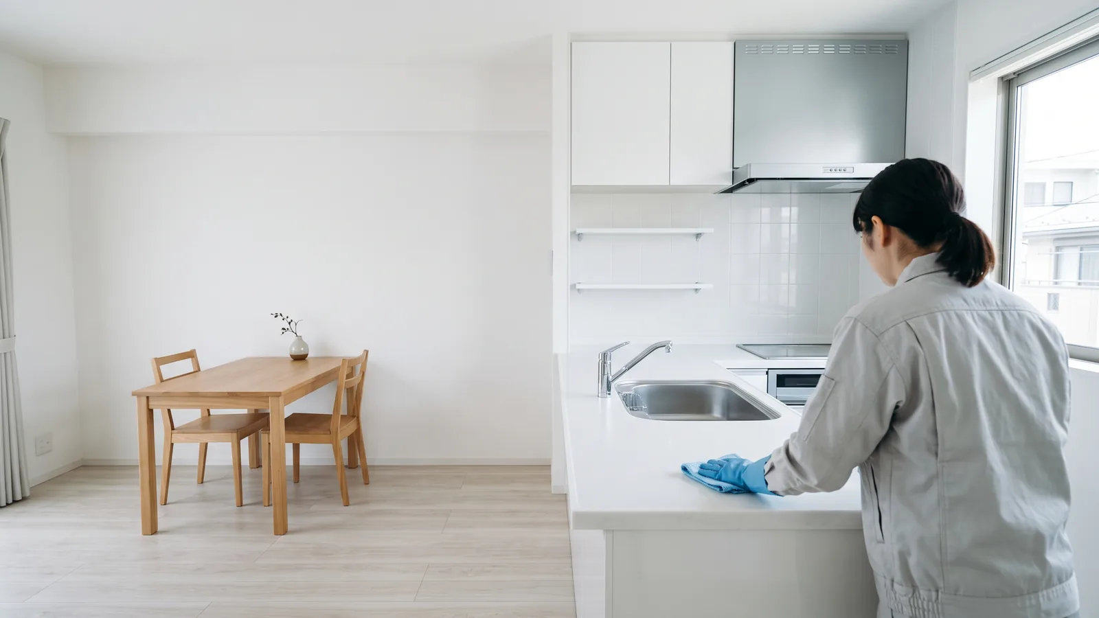 掃除を終えたマンションのキッチンで、作業員が布で調理台を拭いている後ろ姿
